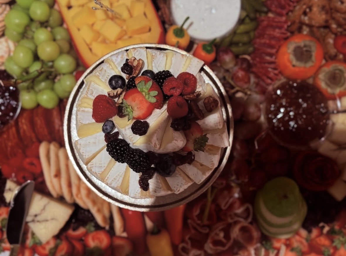 A beautifully styled brie cheese wheel topped with fresh berries and nuts, surrounded by an abundant grazing spread